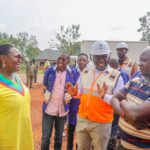 Minister of Energy and Mineral Development Hon. Ruth Nankabirwa (left, in yellow) and UEDCL Managing Director Paul Mwesigwa (in orange reflector jacket) speak to George Sibewalwa (in striped shirt), a shop owner who got a new connection to his shop in Bukomero, Kiboga District on Sunday, August 17, 2025.