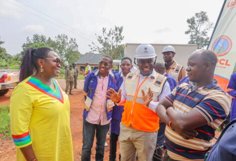 Minister of Energy and Mineral Development Hon. Ruth Nankabirwa (left, in yellow) and UEDCL Managing Director Paul Mwesigwa (in orange reflector jacket) speak to George Sibewalwa (in striped shirt), a shop owner who got a new connection to his shop in Bukomero, Kiboga District on Sunday, August 17, 2025.