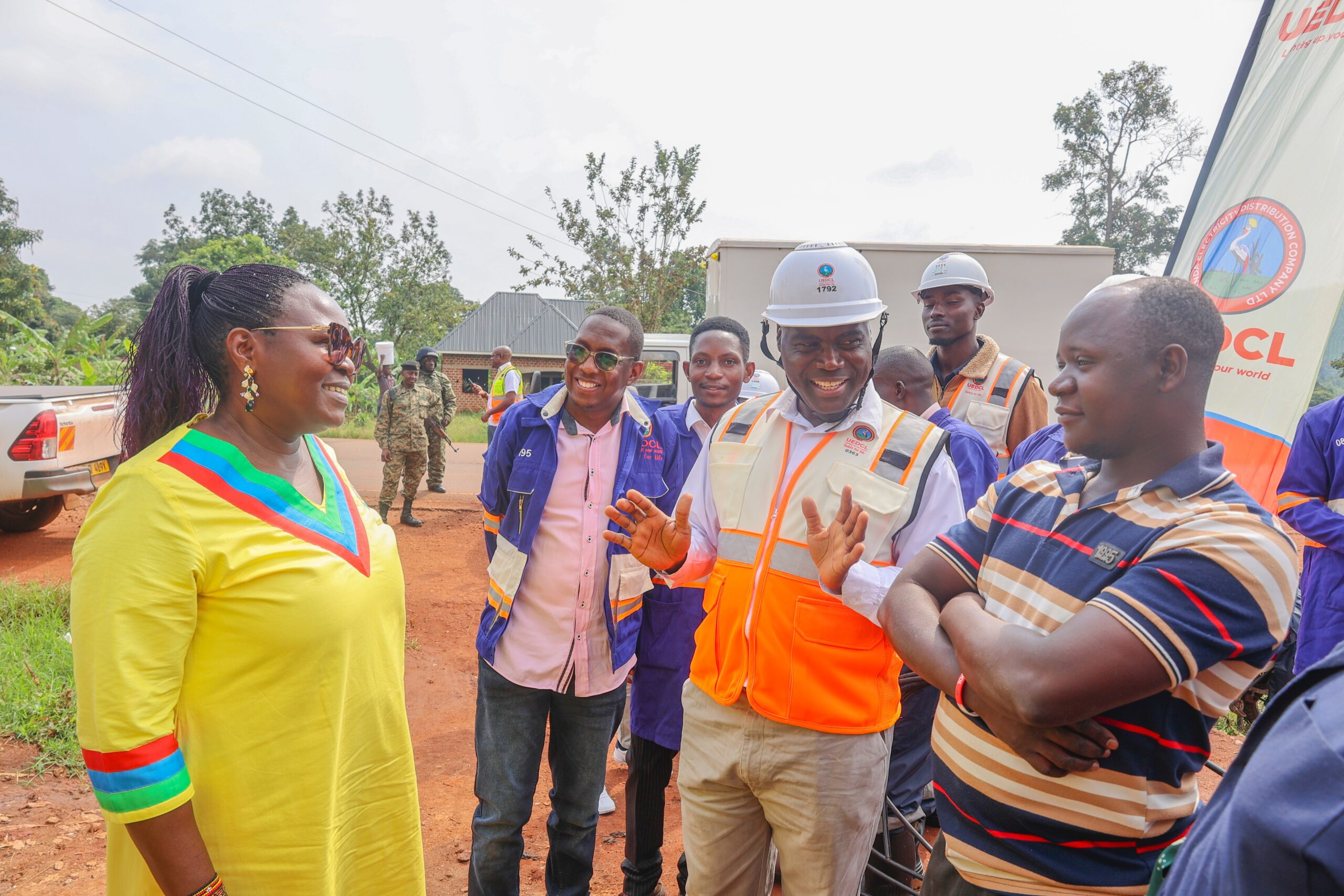 Minister of Energy and Mineral Development Hon. Ruth Nankabirwa (left, in yellow) and UEDCL Managing Director Paul Mwesigwa (in orange reflector jacket) speak to George Sibewalwa (in striped shirt), a shop owner who got a new connection to his shop in Bukomero, Kiboga District on Sunday, August 17, 2025.